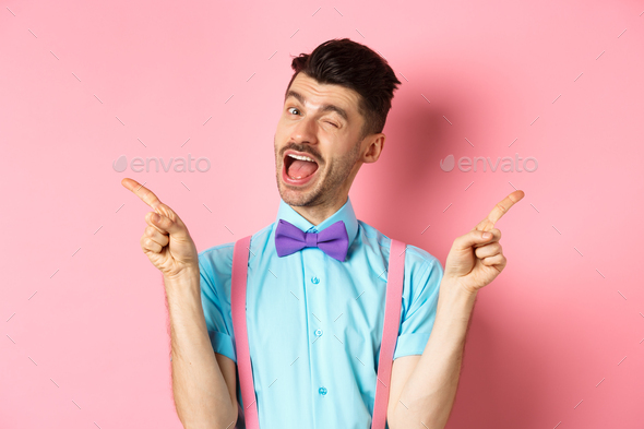 Cheerful young man smiling and winking, showing two sides, pointing fingers sideways and