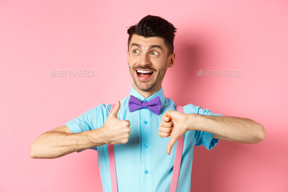 Cheerful man looking happy left, showing thumbs up down, judging product, give positive and negative