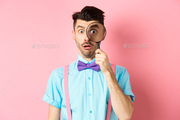 Funny guy look through magnifying glass with surprised face, seeing something interesting, standing