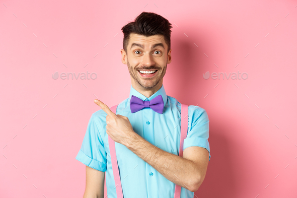 Portrait of handsome happy man showing logo, pointing left and smiling at camera, recommending shop