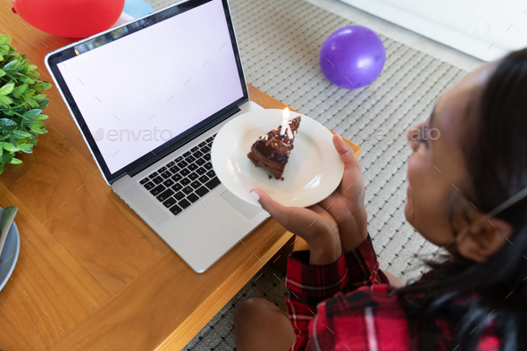 Mixed race woman holding birthday cake using laptop for video chat