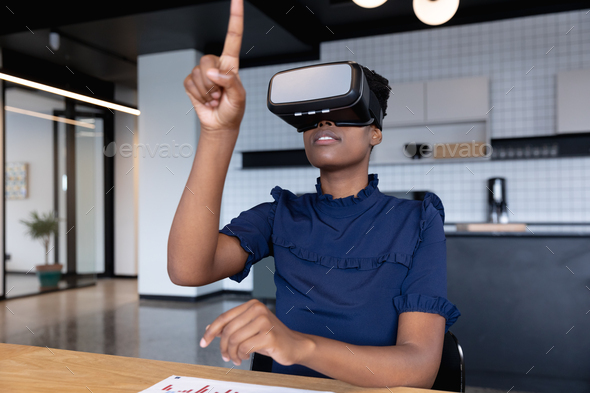 Mixed race businesswoman sitting using vr googles in modern office - Stock Photo - Images