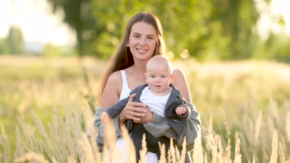 Happy young mum and baby walking together outdoor enjoy beautiful field of sunshine and spring grass