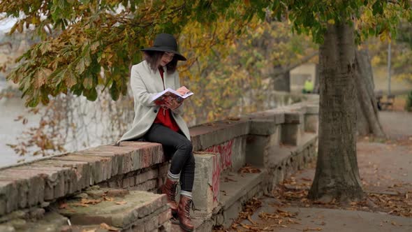 Young Attractive Woman Reading Book in Park By the River at Autumn Day alt