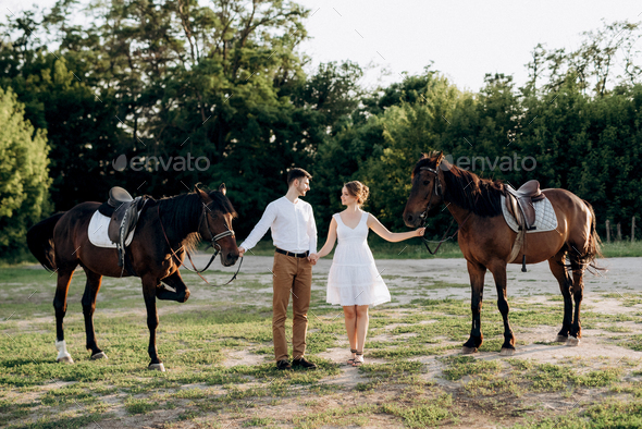 girl in a white sundress and a guy in a white shirt on a walk with brown horses