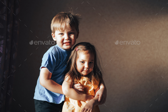 The brother hugs his sister carefully. The sun's rays fall on children. Raising and caring for