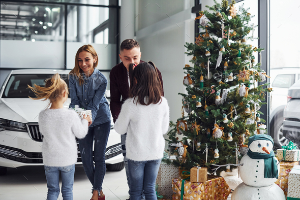 Happy family stands together in salon with car behind and christmas tree