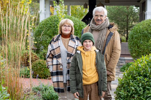 Happy boy and his grandparents standing in front of camera in the garden