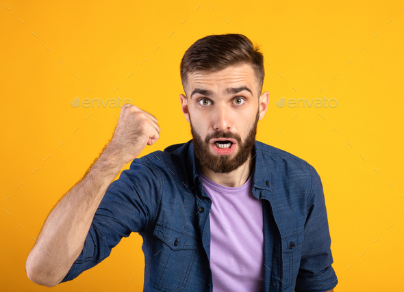 Portrait Of Young Angry Guy Shaking Clenched Fist At Camera And