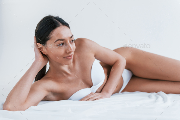 Young woman in underwear and with nice body shape lying down in the studio  against white background Stock Photo by mstandret