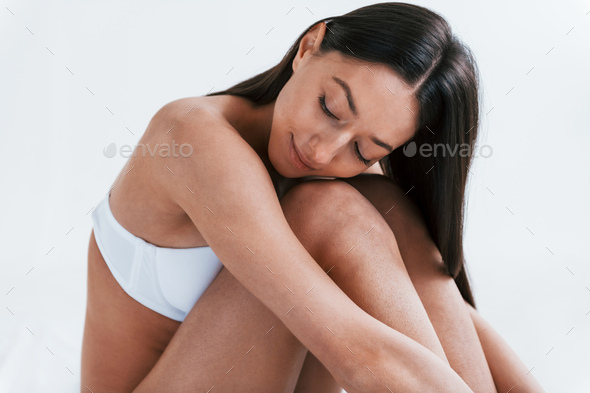 Young woman in underwear and with nice body shape sits in the studio  against white background Stock Photo by mstandret