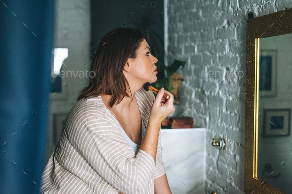 Beautiful woman plus size body positive in home clothes with make up brush in the bathroom