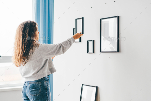 woman with long loose flowing curly hair hangs different picture frames of various size on wall