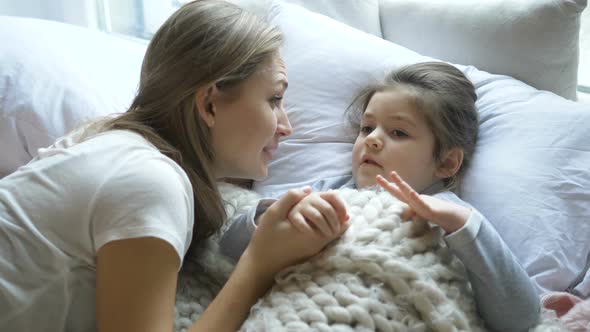 lady with fair hair talks to small child under blanket alt