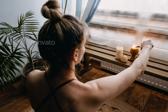 Young woman sitting on the floor, lights candles, enjoy meditation, do yoga exercise at home. Mental - Stock Photo - Images