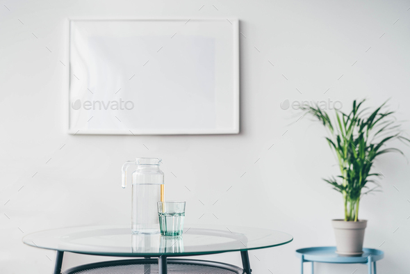 Glasses and carafe with water on table in empty room.
