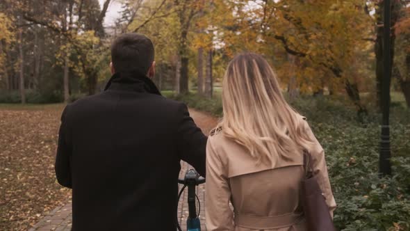 Handsome young couple in the autumn park with electrical bicycle