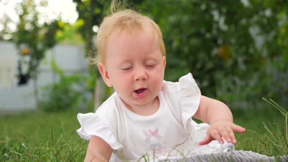Toddler playing in the garden. Baby in white dress lying on green grass. Blue eyed girl outdoor.