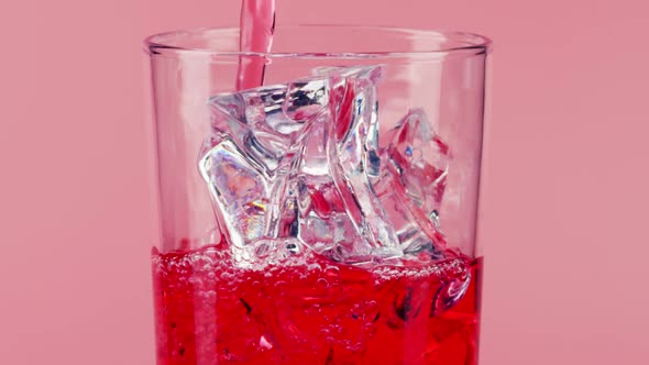 Pouring Red Soft Drink Into a Glass with Ice Cubes alt