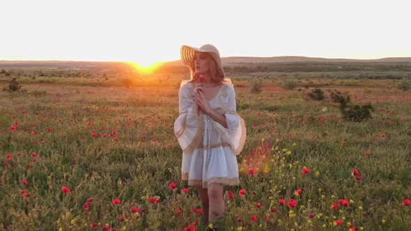 A Young Woman in a White Dress and Hat Walks Through the Field of Wild Poppies with a Flower in Her alt
