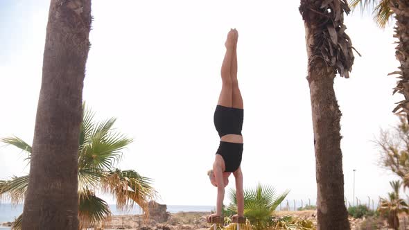 A Young Blonde Woman Standing on the High Beams with Her Hands and Moving Her Legs alt