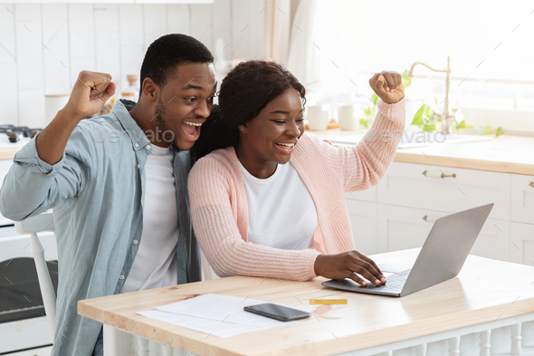 Lucky Winners. Excited african american couple with laptop in kitchen celebrating success