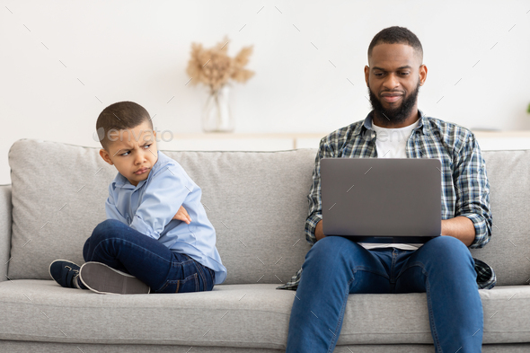 Indifferent African Father Using Laptop Ignoring Offended Son At Home