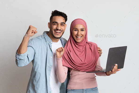 Lucky Winners. Euphoric muslim couple celebrating success with laptop computer