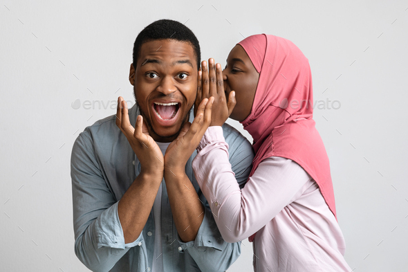 African american muslim woman whispering something to her amazed boyfriend