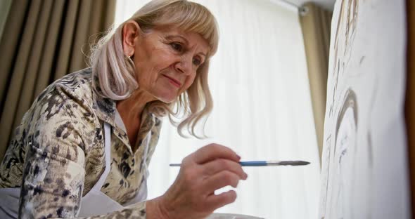 Grandmother Old Woman Is Creative Happy Paints a Picture with Paints and a Brush at Home Alone alt