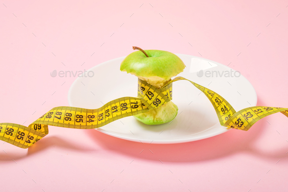 Apple core with measuring tape in place of the waist on a white plate on pink background. Diet - Stock Photo - Images