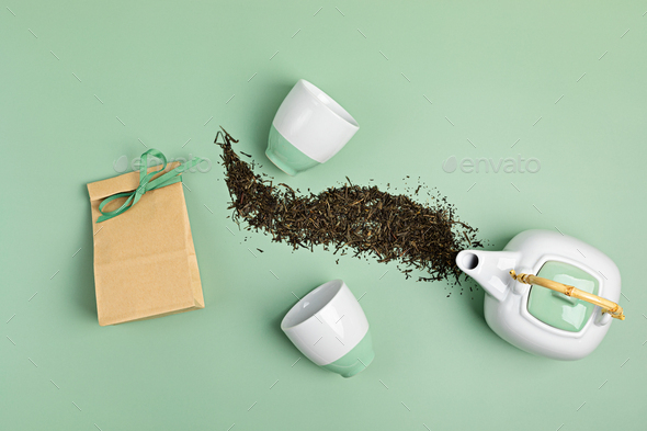 White ceramic tea pot with dry green tea leaves and paper bag on pastel background. Eco friendly