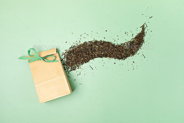 Dry green tea leaves and paper bag on pastel green background. Eco friendly organic brand concept