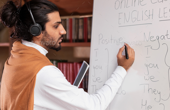 Teacher Man Wearing Headphones Writing English Rules On Blackboard Indoors