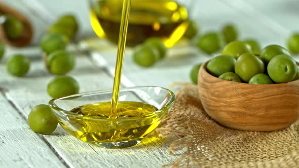 Super Slow Motion Shot of Pouring Fresh Olive Oil Into Glass Bowl on White Wooden Table at 1000 Fps alt