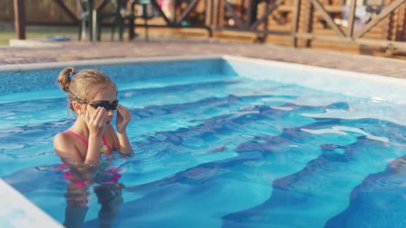 A Girl in a Bright Swimsuit with Swimming Goggles Dives Into a Pool with Clear Transparent Water alt