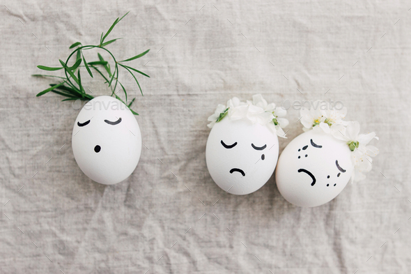 Easter concept. Natural eggs with sad crying and calm faces in cute floral wreaths on linen fabric