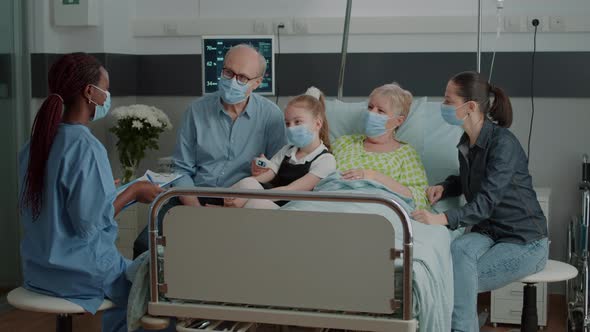 Nurse Giving Assistance to Ill Woman at Visit with Family in Hospital Ward alt