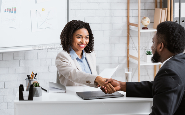 Positive female personnel manager and black job applicant shaking hands before employment interview