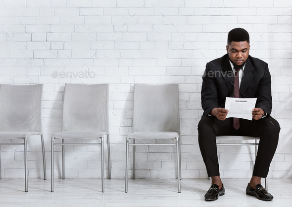 Millennial black man reading his resume while waiting for job interview at office hall, empty space