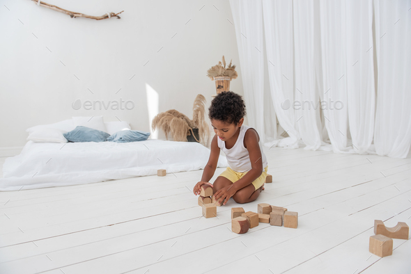 Little happy boy African American play houses with wooden eco bricks, build and destroy towers