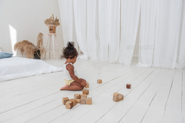 Little beautiful girl African American play houses with wooden eco bricks build and destroy towers