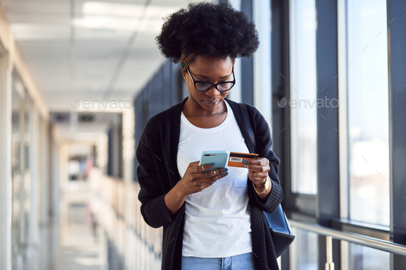 Young african american female passanger in casual clothes is in airport holding credit card
