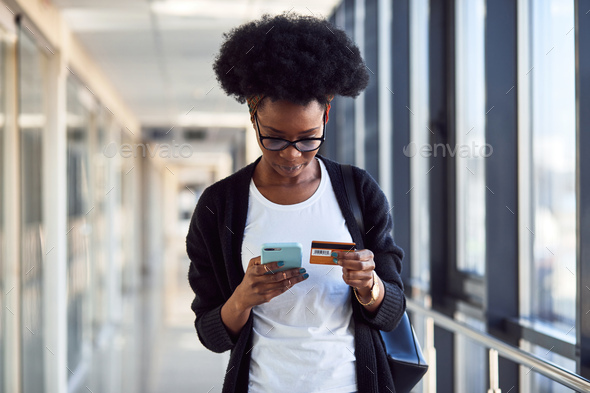 Young african american female passanger in casual clothes is in airport holding credit card