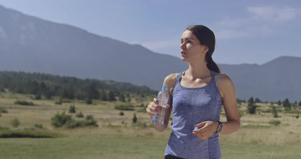 Slow Motion Shot of Sporty Trail Running Woman While Drinking Water and Resting From Intense Jogging alt