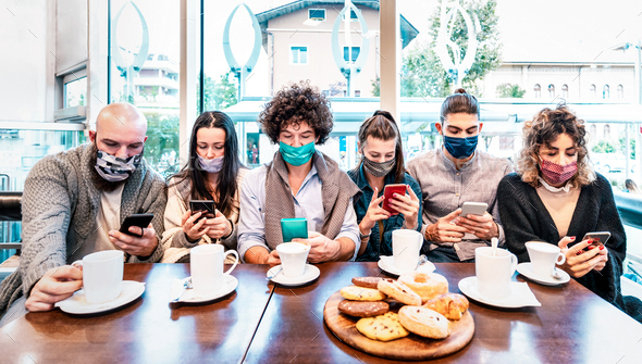 People using mobile smart phones at coffee bar covered by face masks