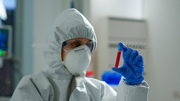 Biochemist in coverall holding blood sample analysing chemical reaction