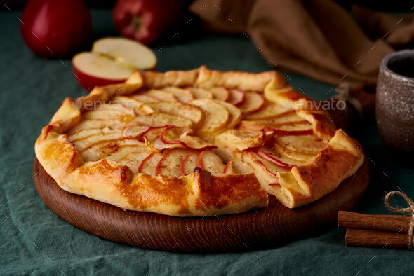 Apple pie, galette with fruits, sweet pastries on dark green tablecloth, close up, side view