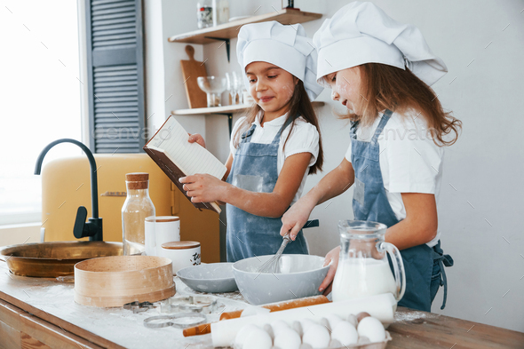 Two little girls in blue chef uniform preparing food on the kitchen and reading receipt book