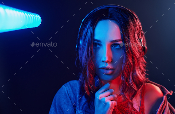 Portrait of young girl that listening to music in headphones in red and blue neon in studio